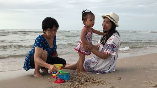 Smiling mother sitting with baby girl playing on shore at beach