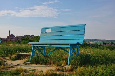 Empty bench on field against sky