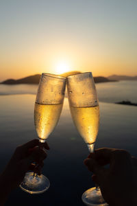 Close-up of hand holding wineglass against sky during sunset