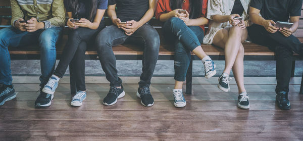 Low section of people using mobile phones while sitting on bench