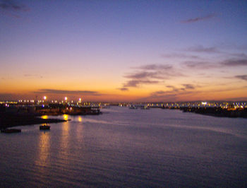 River by illuminated city against sky at sunset