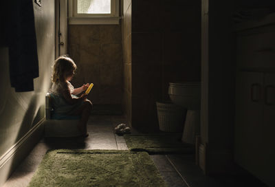 Side view of baby girl on potty while holding popsicle in darkroom at home