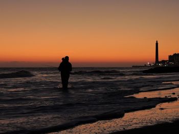 Silhouette man standing in sea against clear sky during sunset