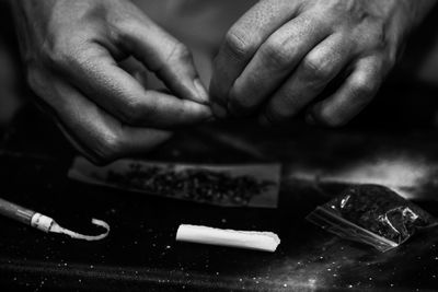 Cropped hand of woman making marijuana joint on table