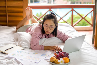 Young businesswoman using laptop while lying on bed