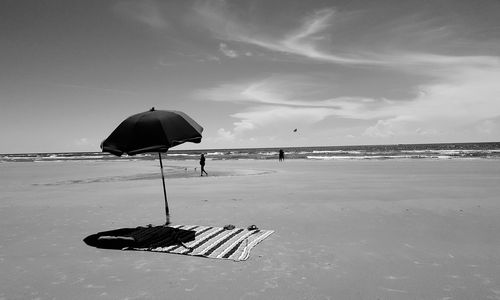 Beach umbrella and blanket on beach against sky