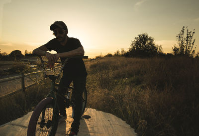 Man with bicycle on field against sky during sunset