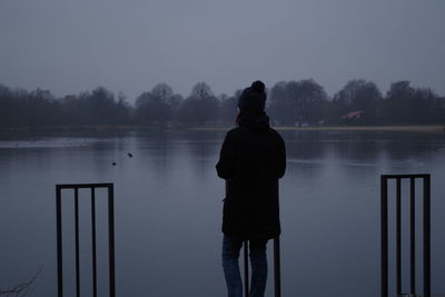 Rear view of silhouette man standing by lake against sky