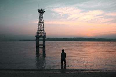 Rear view of silhouette man standing by sea against sky