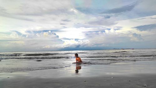 Vew of little boy playing sand at beach against sky