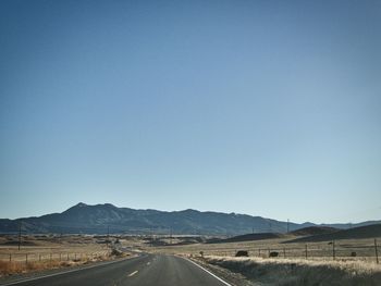 Road by landscape against clear blue sky