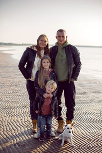 Family in a leather jacket walks along the beach with their dog in autumn