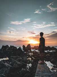 Rear view of man standing on rock against sky during sunset