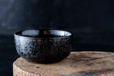 Close-up of black bowl on tree stump against black background