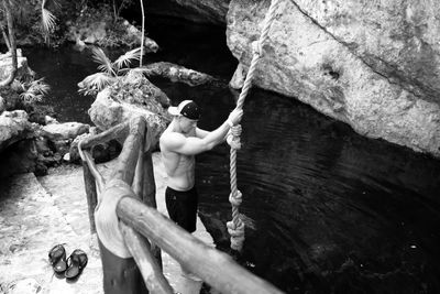 High angle view of shirtless muscular man holding rope by pond