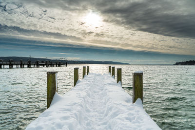 Wooden posts in sea against sky during winter