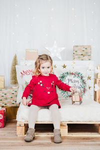 Smiling little girl wearing red christmas dress at home over christmas decoration. holiday concept