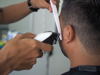 Cropped hands of barber cutting male customer hair in shop