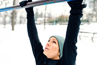 Close-up of woman doing chin-ups over snow covered field