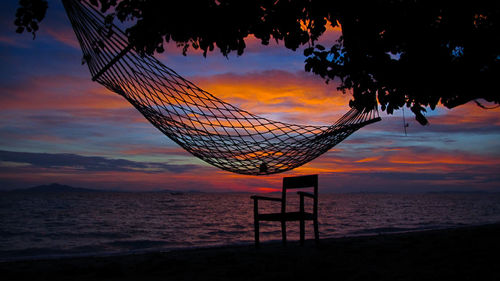 Hammock hanging at beach against cloudy sky during sunset