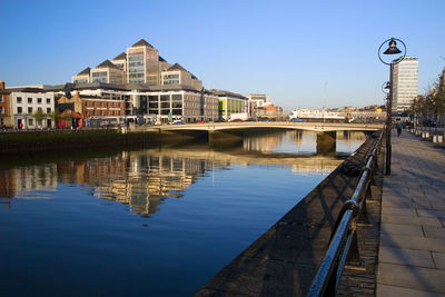 Bridge over river by buildings against clear blue sky