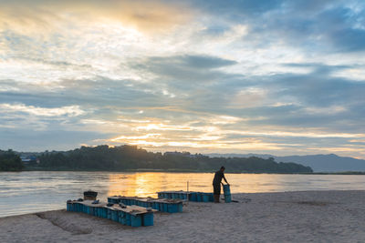 Silhouette people standing on shore against sky during sunset