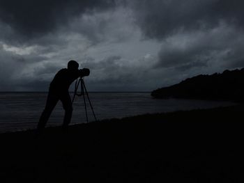 Silhouette of people standing on beach against cloudy sky