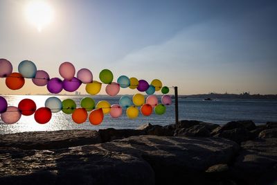 Multi colored balloons on rock by sea against sky