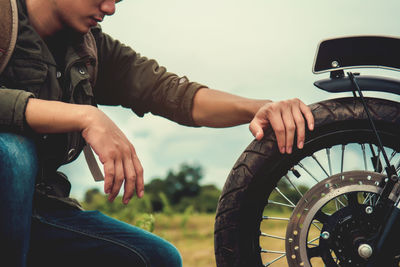 Side view of young man looking at tire of motorcycle