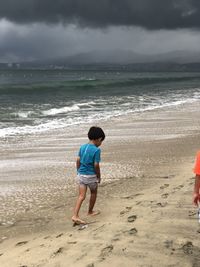 Rear view of boy on beach against sky