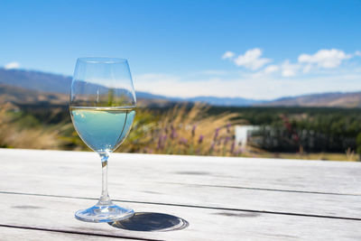 Close-up of wineglass on table against blue sky