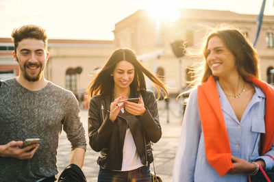 Happy young woman holding smart phone standing in city