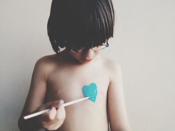 Shirtless boy painting heart shape on chest at home