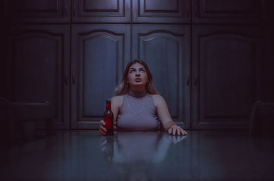 Young woman looking up while holding bottle on table