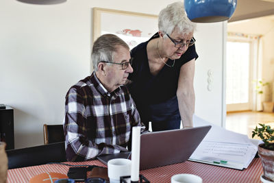 Senior couple with laptop at and financial bills at dining table