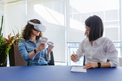 Two colleagues women sitting at the table in the office with vr helmet