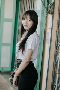 Portrait of smiling woman standing against wall