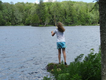 Rear view of girl standing by sea against trees