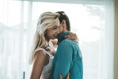 Couple embracing against window at home