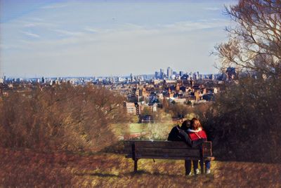 Woman sitting in park by cityscape against sky