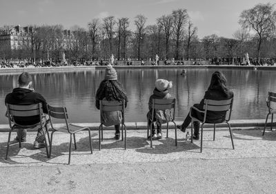 Rear view of people sitting on chair by lake