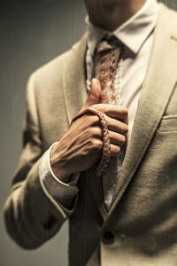 Midsection of businessman holding tentacle necktie while standing against gray background