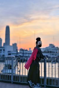 Person standing by railing against sky during sunset
