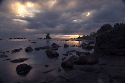Rocks on beach against sky during sunset