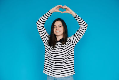 Portrait of young woman standing against blue background