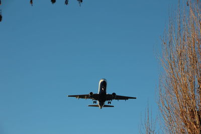 Low angle view of airplane flying against clear blue sky