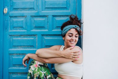 Portrait of smiling young woman standing against door