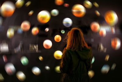 Rear view of woman standing against defocused spheres