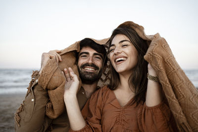 Cheerful young couple covering blanket at beach