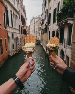 Cropped hands of people holding ice cream cones against canal